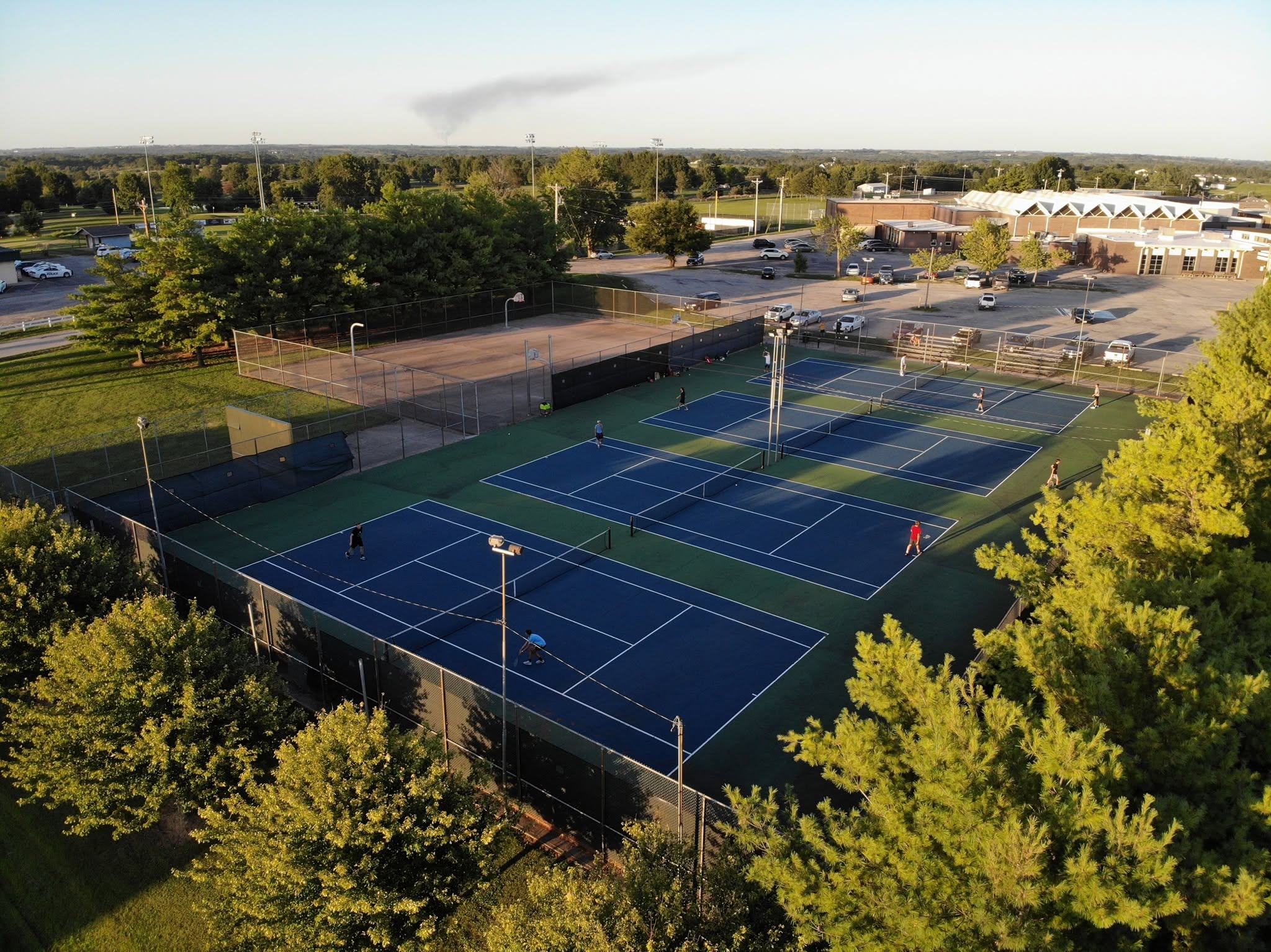 Aerial photograph of players on the existing outdoor courts, with school buildings in the background